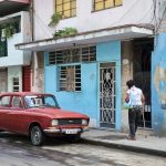 a woman walking in a street in la Havana Cuba on the side walk by a red parked car