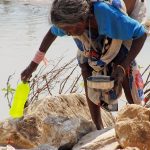 a local older woman is filing up a plastic bottle in the Narmada river at Marble Rocks in India