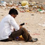 man looking at his phone as he is sitting in the plastic on the Versova Mumbai beach before the clean-up