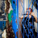 an old woman with red hair watching the street view from inside her house like behind bars in callejon de hamel la havana cuba